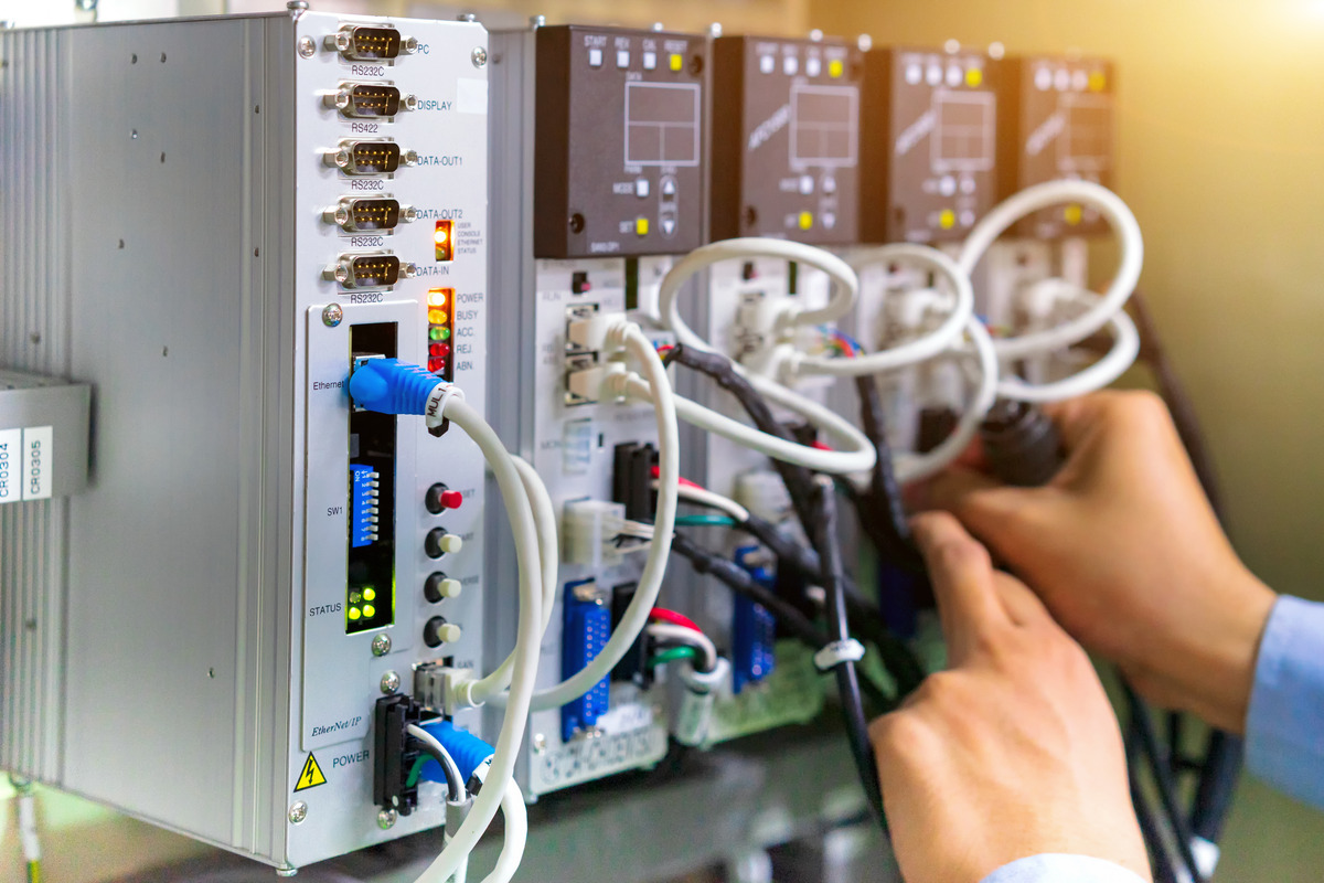 Two hands plugging in an RS232 smart cable to the back of a large control box of an automation machine.